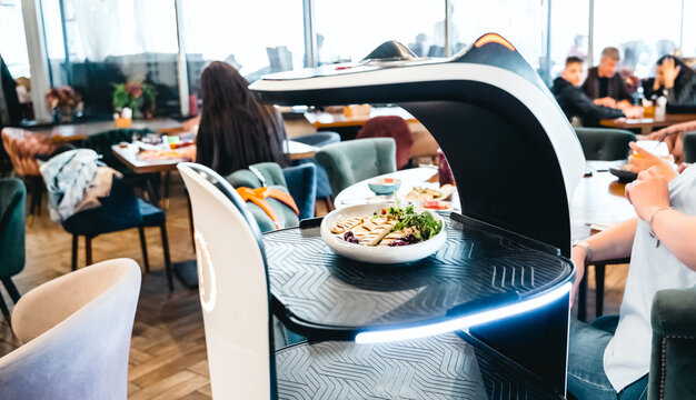 Robot waiter serve food at modern restaurant table.Offering innovation futuristic high-tech automated dining experience.Bringing,delivery automation order to customer.Digital robotic AI smart service