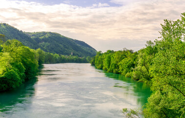 Fototapeta na wymiar beautiful landscape of spring or summer sunset river with blue water and green hills on sides and mountains with amazing cloude sky on background