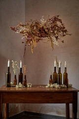 Decorated table with bottles and candles under bunch of dried flowers