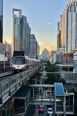 Electric train parallel to the road with cars traffic in the middle of Bangkok in the evening.