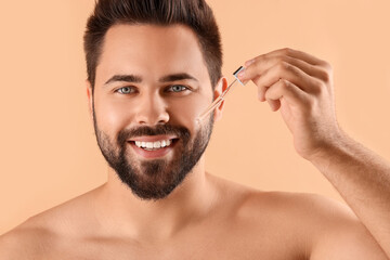 Obraz premium Handsome man applying cosmetic serum onto face on beige background