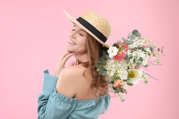 Beautiful woman in straw hat with bouquet of flowers on pink background