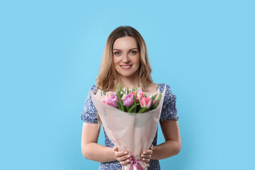 Happy young woman with bouquet of beautiful tulips on light blue background