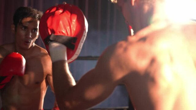 Asian and Caucasian Muay Thai boxer unleash punch in fierce boxing training session, delivering punching strike to sparring trainer, showcasing Muay Thai boxing technique and skill. Impetus