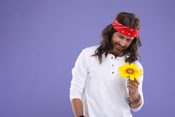 Stylish hippie man with sunflower on violet background, space for text