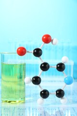 Molecular model and laboratory glassware against light blue background