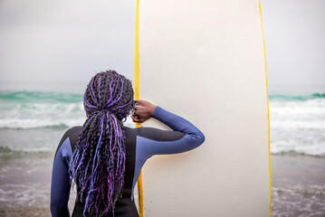 Black Jamaican Surfer Wearing Neoprene View from Back Holding Her Board While Watching the Sea to...