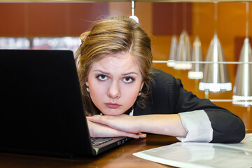 Young beautiful tired sad blonde woman laying on a table with laptop, resting on her working place in the office.