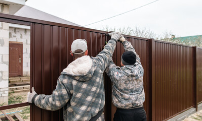 Workers install a metal profile fence