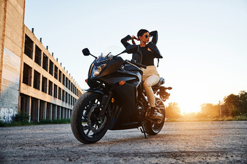 Building behind. Woman is with motorcycle outdoors