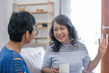 Fototapeta premium Two Asian women are sitting drinking coffee and chatting in the living room.