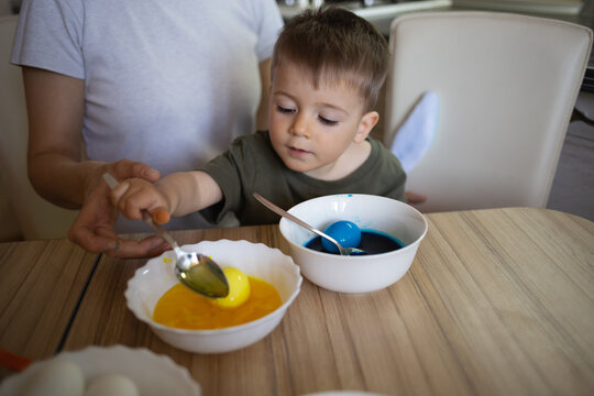 little cute boy paints eggs for easter sitting in the kitchen at the table
