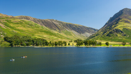 Fototapeta na wymiar Kayaks and paddleboards on a calm, peaceful lake surrounded by tall mountains (Buttermere, Lake Distrtict)