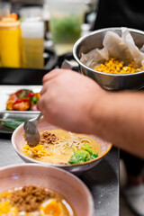 chef cooking Asian noodle soup, ramen with chicken, tofu, vegetables and egg in bowl