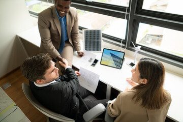 High angle view of diverse group of business people working together in office, Brainstorming on how to use natural energy from wind and sunlight to offer customers.
