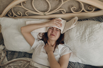 Young woman with headache flu ill sick disease cold at home indoor lying on bed with cold compress...