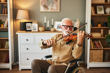 Elderly man in the wheelchair playing the violin at home