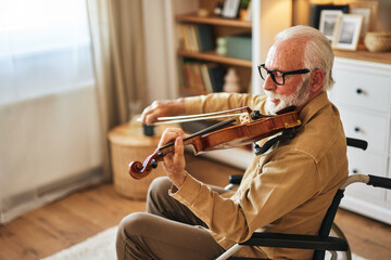 Elderly man in the wheelchair playing the violin at home © Stockphotodirectors