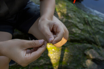 The hands of a teenager trying to put worms on a hook for fishing. Sport fishing on the river in...