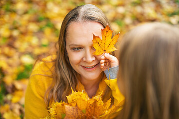 Autumnal mood. Little child girl play with mother in autumn orange leaves, outdoor.