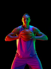 Handsome teen boy, basketball player in uniform standing with ball and smiling against black studio background in neon light. Concept of professional sport, competition, hobby, game, competition © master1305