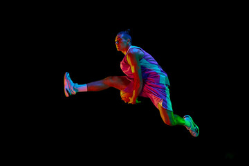 Competitive teen boy in motion, playing, training basketball, jumping with ball against black...