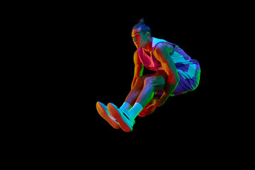 Young sportive athlete, basketball player in motion jumping with ball against black studio...