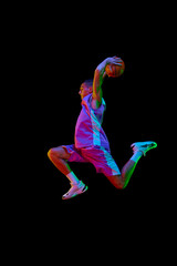 Scoring winning goal. Young man in uniform playing basketball, jumping with ball against black...