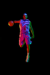 Scoring winning goal. Young man in uniform playing basketball, jumping with ball against black...