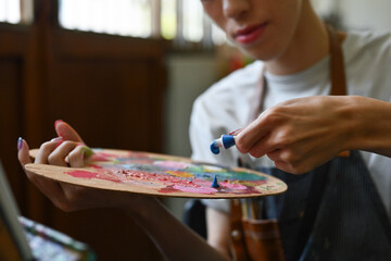 Selective focus of an Asian male teenager hand squeezing a tube of acrylic watercolor into the palette