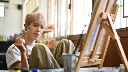 Portrait image of LGBT artist, an Asian male teenager with colored hair doing artwork in the workshop studio