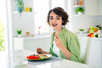 Photo of adorable pretty girl wear green shirt biting tasty meat piece indoors kitchen room