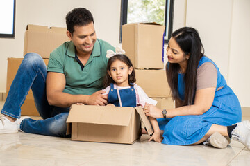 Happy young indian family with kid having fun in new home. Playing with boxes, Real estate, residential mortgage, moving into dream house concept.