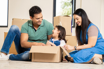 Happy young indian family with kid having fun in new home. Playing with boxes, Real estate, residential mortgage, moving into dream house concept.