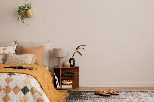 Minimalist composition of bedroom interior with copy space, bed, orange bedding, wooden bedside table, patterned rug, plants, stylish lamp, slippers and personal accessories. Home decor. Template.