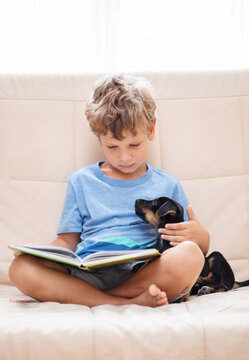 A boy with a little dog is reading a book