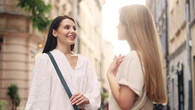 Smiling positive young female friends emotionally talking gossiping relaxing together while meeting at city street Pretty women sharing last news after not seeing each other for long time outdoors