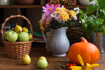 Autumn still life with pumpkin. Flowers and apple harvest in a wicker basket, orange ripe pumpkins on the table