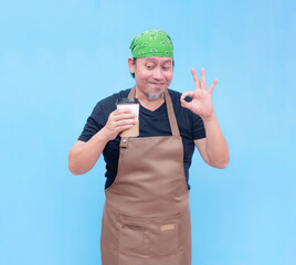 A happy middle-aged barista holding a cup of coffee to-go on one hand and looking at it while doing...
