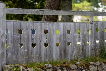 Une clôture en bois avec des décorations de fleurs, la clôture est posée sûr un mur en pierre