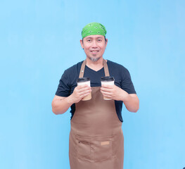 A smiling middle-aged barista holding a cup of coffee to-go in each hand. Isolated on a blue...