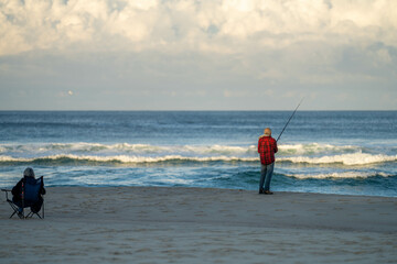 man beach fishing in the ocean waves at dusk