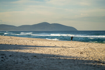 man beach fishing in the ocean waves at dusk