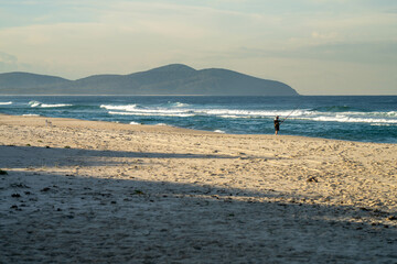 man beach fishing in the ocean waves at dusk