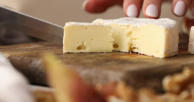 Female hands cutting brie cheese. Cheese with white mold. Preparing antipasto. Food close-up.