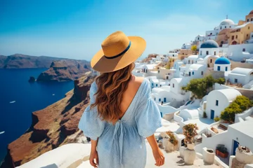 Deurstickers Woman in blue dress and hat looks out over the white village of oia. © valentyn640