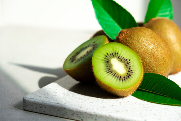 Ripe kiwi fruits in sunlight. Heap of whole kiwi fruits with green leaves and fresh cut kiwi on...