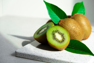 Ripe kiwi fruits in sunlight. Heap of whole kiwi fruits with green leaves and fresh cut kiwi on...