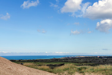 Panorama of sand dunes and blue sea. Seascape with people resting and walking near the sea on a summer day.