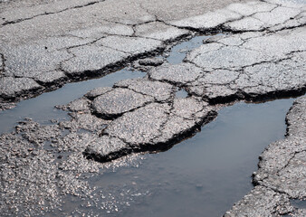 Potholes on bad asphalt road. Closeup - obrazy, fototapety, plakaty